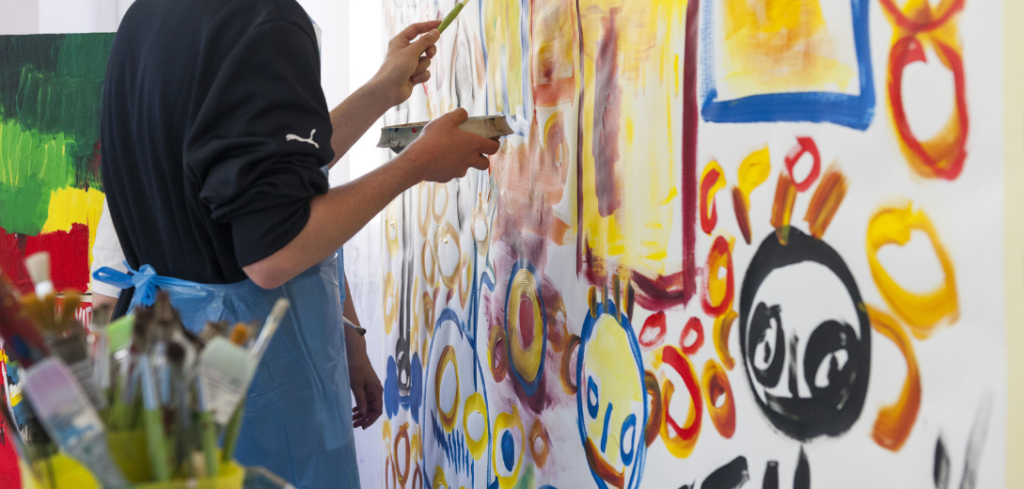 Persona dipinge su tela con colori vivaci e pennelli.
