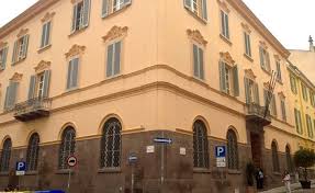 Edificio storico color pesca con finestre blu e balcone, situato in un angolo strada con segnaletica stradale visibile.