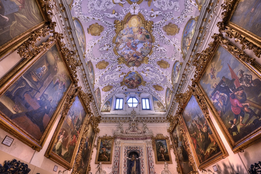 Interno di una chiesa con affreschi dettagliati sul soffitto e dipinti storici sulle pareti.